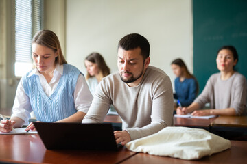 Woman and man university students sitting at table during lesson and using laptop.