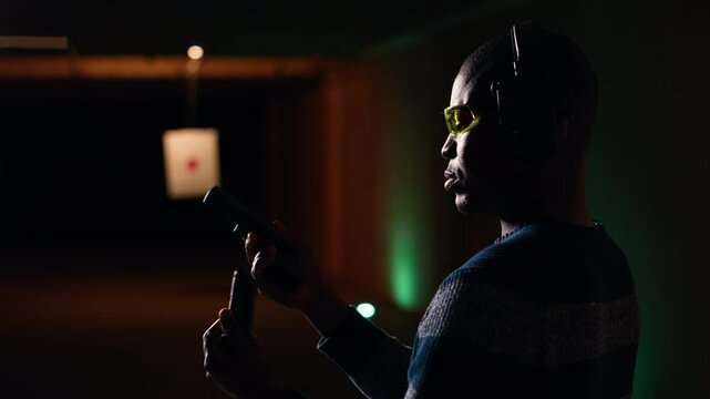 Portrait of happy shooting range customer reloading pistol, shooting targets, having fun. Close up of joyous man at shooting ground facility loading pistol, wearing protection goggles, camera B