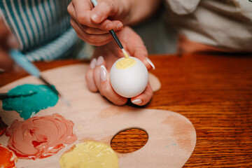 Women painting easter eggs on wooden table with palette and brushes