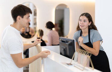 Young female hairdresser stylist at cash register consulting young male client in beauty salon