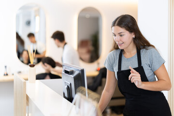 Young female hairdresser stylist stands at cash register in beauty salon