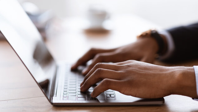 Selective focus on male hands typing on laptop keyboard, cropped, side view. African american businessman sending emails to clients or assistant. Modern technologies and business concept