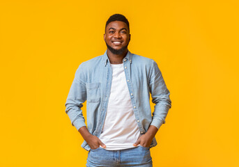Portrait of confident african american man standing with hands in pockets on yellow background with...