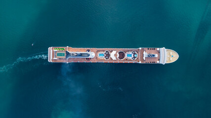 Aerial view of luxurious cruise ship sailing slowly in calm blue water as smoke pours from the...