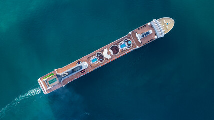 Aerial top down view of luxurious cruise ship sailing slowly in calm blue sea leaving a white trail in the water 