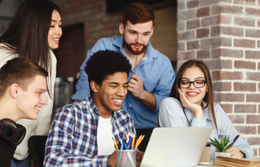 Friends preparing for final exams togehter, sitting in library and using laptop