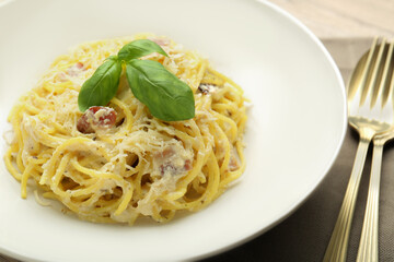 Delicious pasta Carbonara with basil on table, closeup
