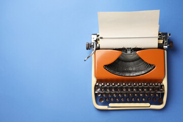 Vintage typewriter with sheet of paper on blue background, top view. Space for text