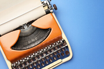 Vintage typewriter with sheet of paper on blue background, top view. Space for text