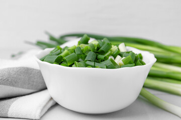 Chopped green onion in bowl and stems on white table, closeup