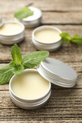 Natural lip balms and mint leaves on wooden background, selective focus