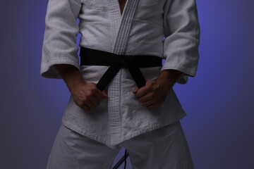 Karate fighter in uniform on dark purple background, closeup