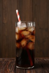 Cold cola with ice cubes and drinking straw in glass on wooden table