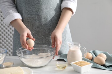 Making cinnamon rolls. Woman adding egg into bowl at white marble table, closeup