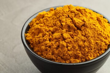 Turmeric powder in bowl on grey table, closeup
