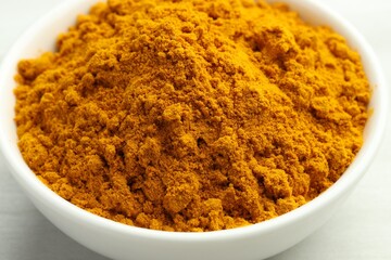 Turmeric powder in bowl on white table, closeup