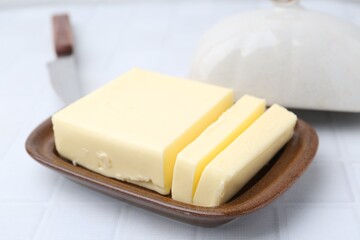 Cut tasty butter in dish on white tiled table, closeup