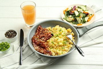 Tasty brunch. Delicious scrambled eggs, bacon, salad and glass of juice served on white wooden table