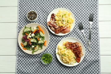 Tasty brunch. Delicious scrambled eggs, bacon and salad served on white wooden table, flat lay