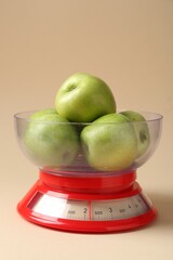 Kitchen scale with apples on beige background, closeup