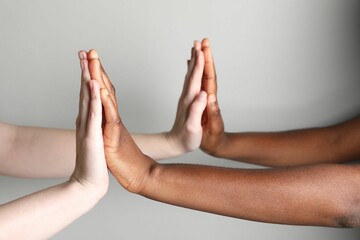 Stop racism. People of different skin colors joining hands on light grey background, closeup