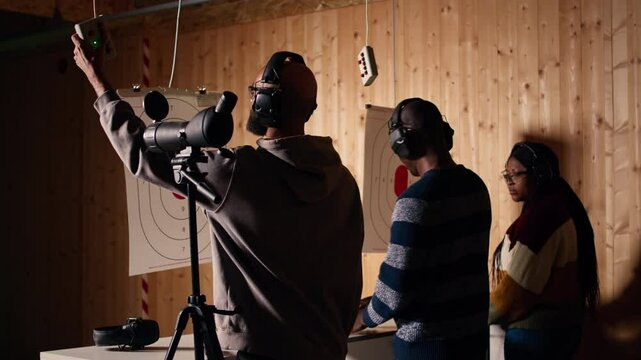 Friends in firing range doing recreational shooting, using magnifying lens to see targets. People training with handguns, sharpening skills, zooming to check points scored on bullseyes, camera A