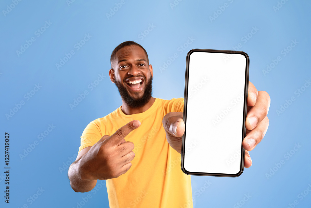 Poster Mobile advertisement. Overjoyed African American man pointing at cellphone with empty white screen on blue studio background, mockup for app or website. Cellphone display template