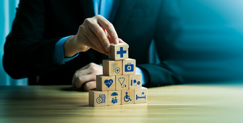 Businessman stacking wooden blocks with healthcare icons, representing medical services, health...