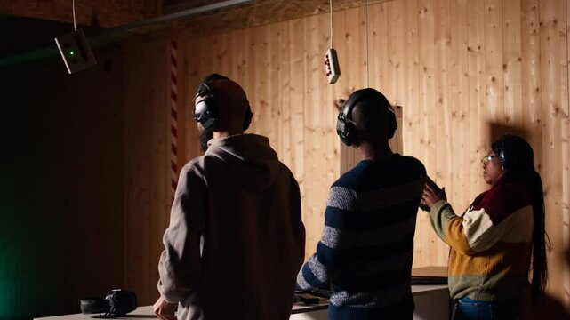 Friends in firing range doing recreational shooting, pressing mechanism to recall paper targets. People training with handguns, sharpening skills, checking points scored on bullseyes, camera A