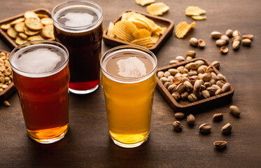 Table for company of friends. Crispy snacks and different types of beer in glasses on wooden background, close up