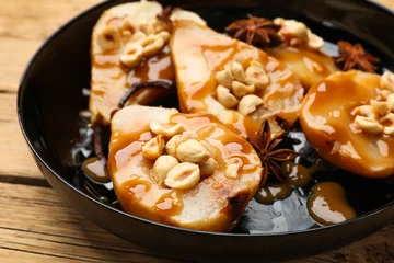 Delicious pears with caramel sauce, nuts and anise stars on wooden table, closeup