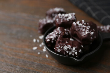 Tasty chocolate candies with salt in bowl on wooden table, closeup. Space for text
