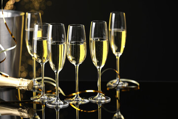 Champagne in glasses and bottle on mirror surface against black background with blurred lights