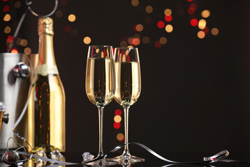 Champagne in glasses and bottle on mirror surface against black background with blurred lights, space for text