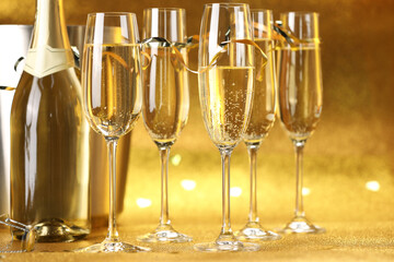 Champagne in glasses, bottle and ice bucket on golden background, closeup