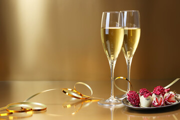 Champagne in glasses and tasty candies on golden background, space for text