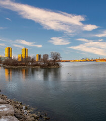 Obraz premium City skyline reflected in calm lake waters, winter trees.