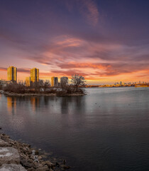 Fototapeta premium Sunset cityscape reflected in calm water, a tranquil scene with city skyline in the background.