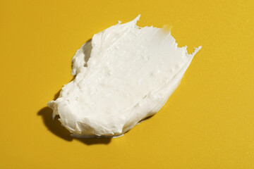 Cream on dark yellow background, closeup. Sample of cosmetic product