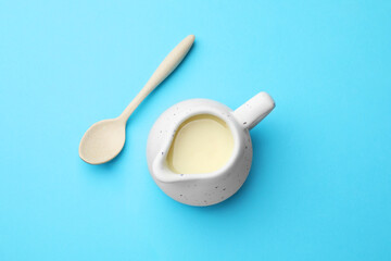 Tasty condensed milk in jug and spoon on light blue background, top view