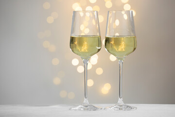 Tasty white wine in glasses on table against grey background with blurred lights, bokeh effect. Space for text