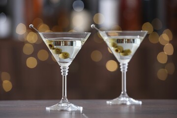 Martini cocktail with olives in glasses on wooden table against blurred background. Bokeh effect
