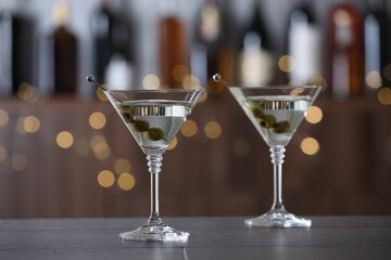 Martini cocktail with olives in glasses on wooden table against blurred background. Bokeh effect