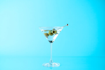 Martini cocktail with olives in glass on light blue background