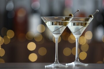 Martini cocktail with olives in glasses on wooden table against blurred background, closeup. Bokeh effect