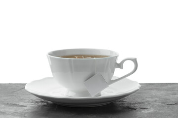 Tea bag in cup with hot drink on gray textured table against white background