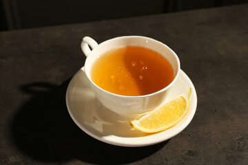 Refreshing green tea in cup and slice of lemon on dark textured table, closeup