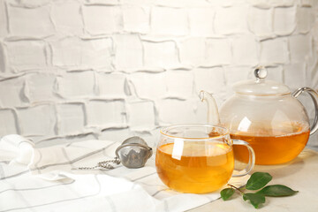 Refreshing green tea, strainer and leaves on light table against textured wall. Space for text