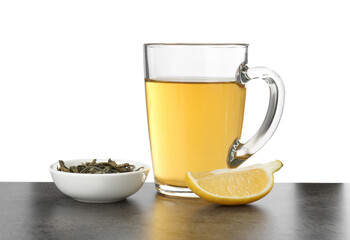 Refreshing green tea in cup, slice of lemon and dry leaves on grey textured table against white...