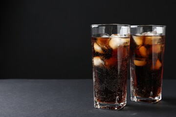 Refreshing cola with ice cubes in glasses on black table, closeup. Space for text